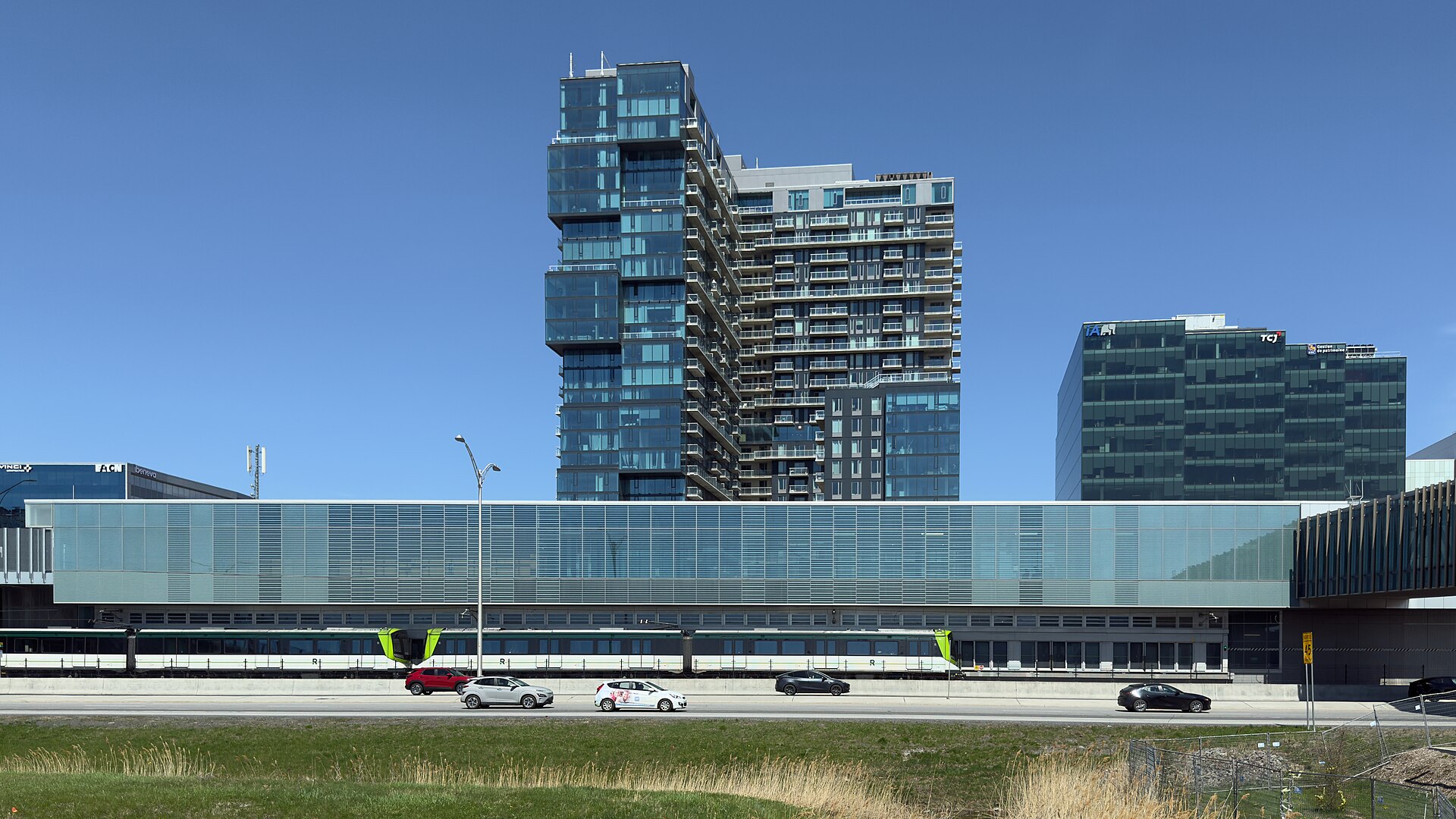 Un train du REM arrive à la station Du Quartier, avec les tours de Solar Uniquartier derrière