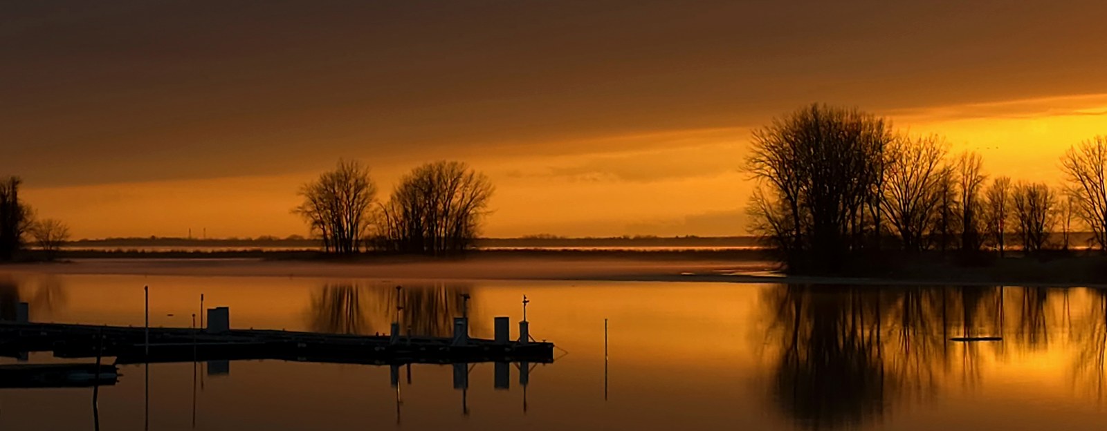 Coucher de soleil doré sur le fleuve Saint-Laurent à Contrecœur, avec les quais de la marina et les îles en silhouette